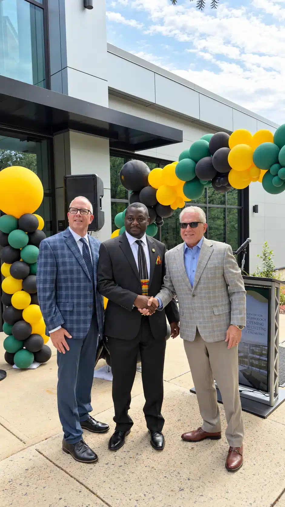 Three guests at the Essex County College Center for Technology opening, with a handshake and green, yellow and black balloons.