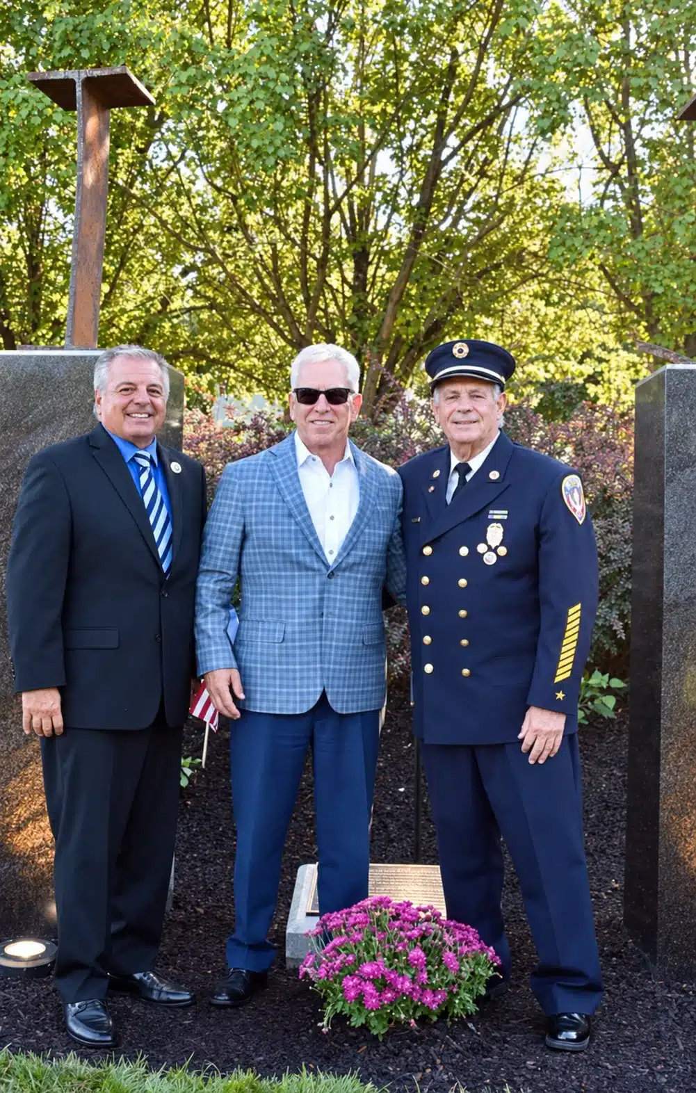 Three attendees beside the steel beams and stone monuments at the Bergen County 9/11 Memorial rededication.